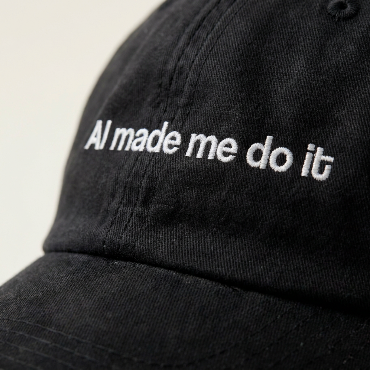 Close-up of the AI made me do it embroidery in white thread on a washed black cotton cap