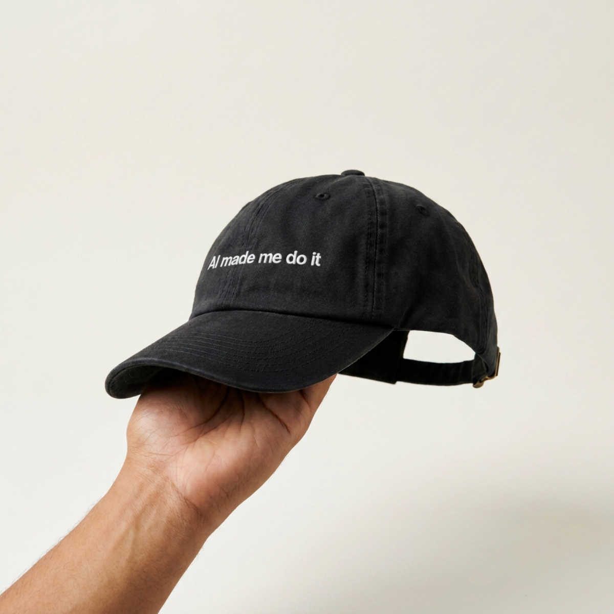 Hand holding up the AI Made Me Do It black cap, side profile with adjustable back strap