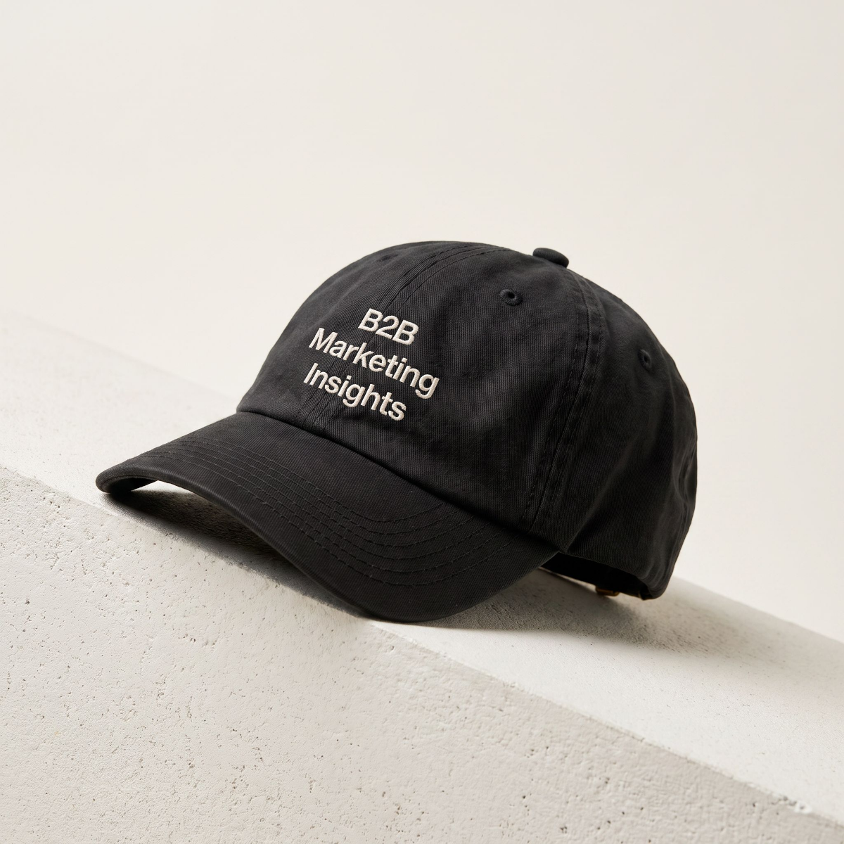 B2B Marketing Insights black dad cap resting on a cream concrete ledge in daylight