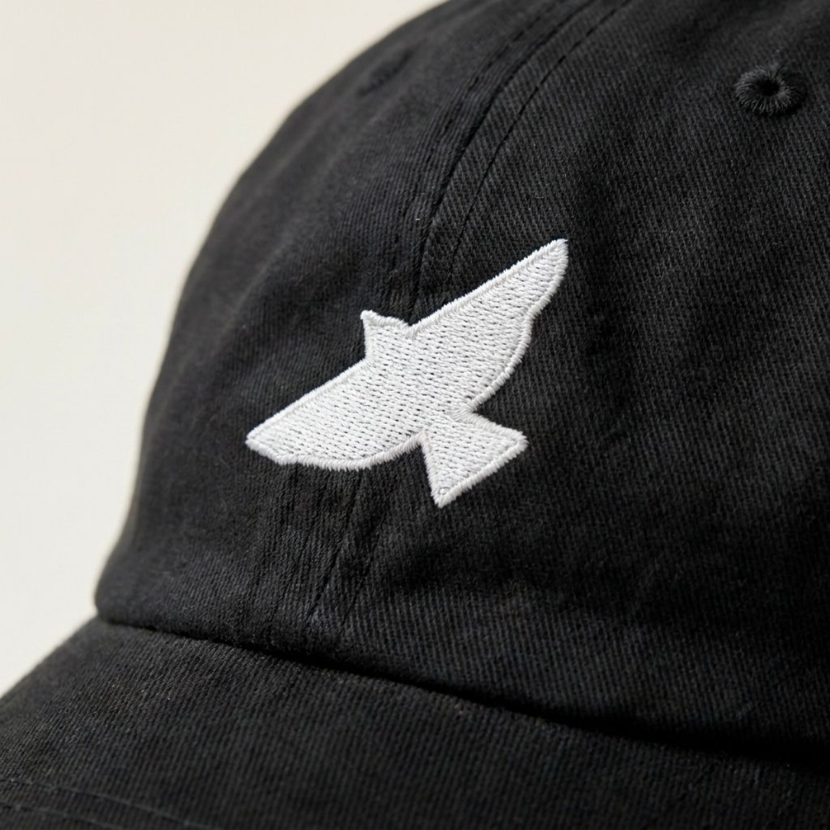 Close-up of the white bird embroidery on the Free as a Bird black cotton cap