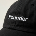 Close-up of the Founder embroidery in white thread on a washed black cotton cap