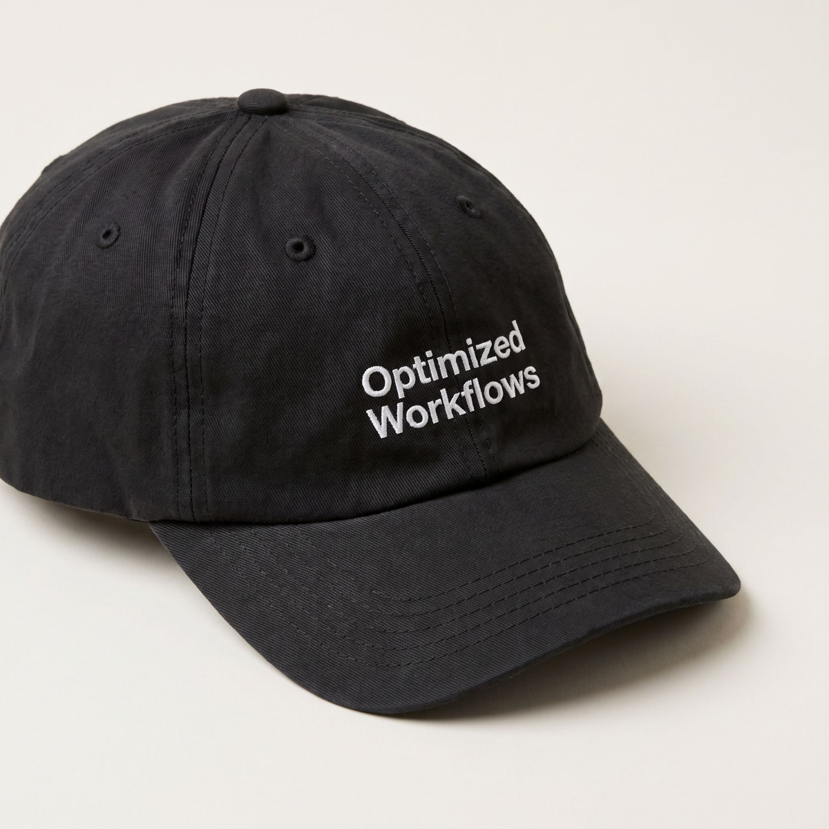 Optimized Workflows black cap at a three-quarter front angle against a cream backdrop
