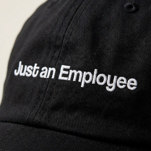 Close-up of the Just an Employee embroidery in white thread on washed black cotton