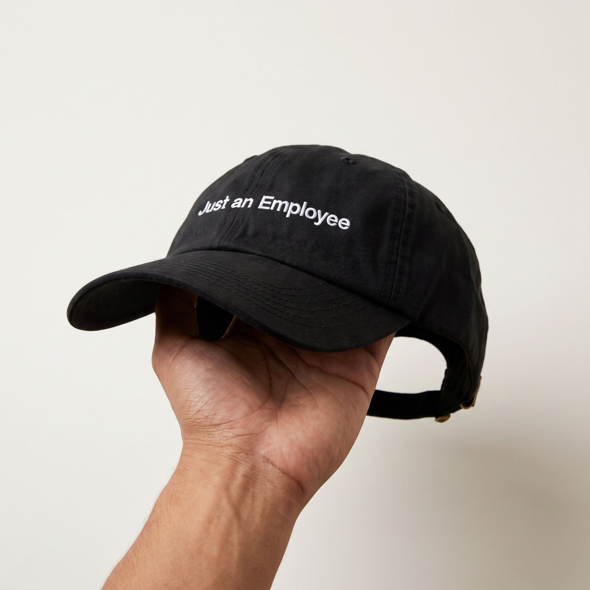 Hand holding up the Just an Employee black dad cap, side profile with back strap