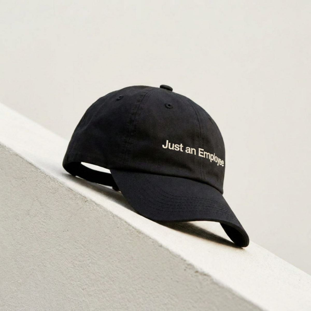 Just an Employee black cap resting on a cream concrete ledge in daylight