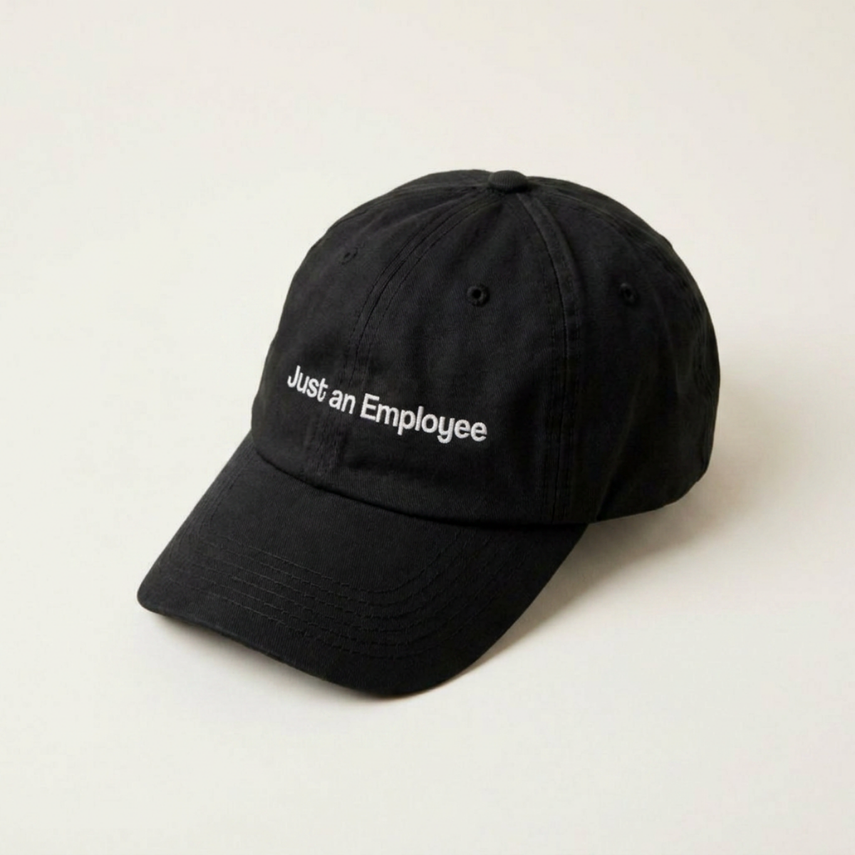 Just an Employee black cap at a three-quarter front angle against a cream backdrop
