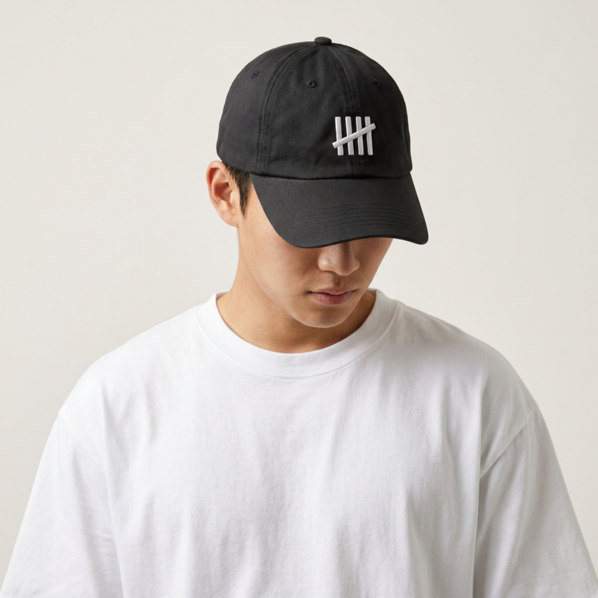 Model in a white tee wearing The HeadCount tally mark logo cap, head tilted down