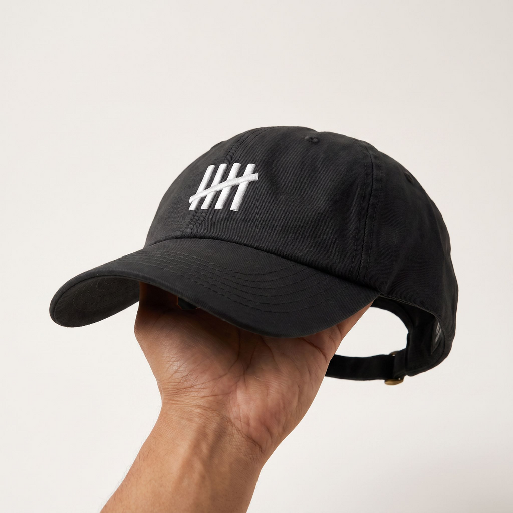 Hand holding up The HeadCount logo cap, showing the curved brim and back strap