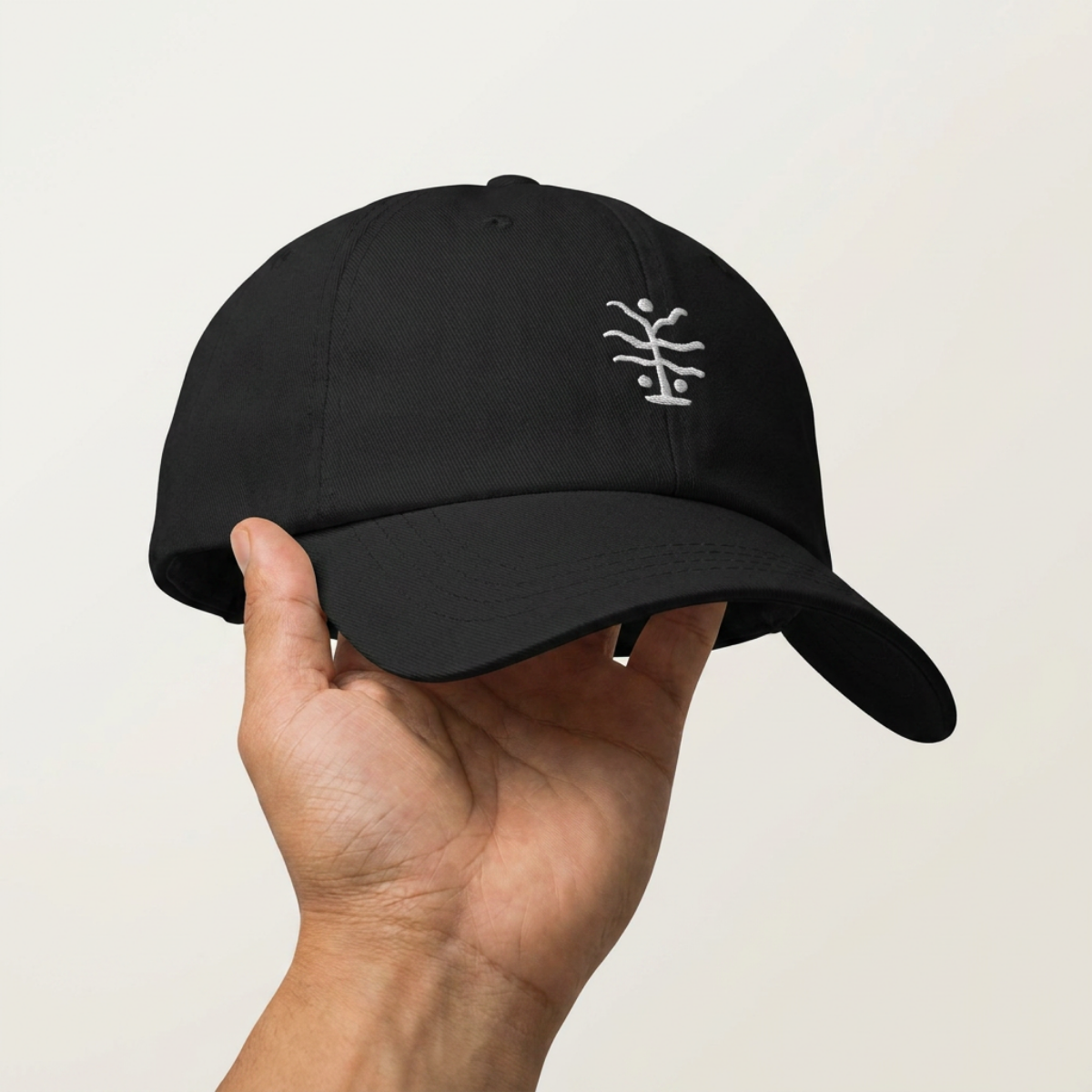 Hand holding the Seaweed Cap, white seaweed embroidery on a black cotton dad cap