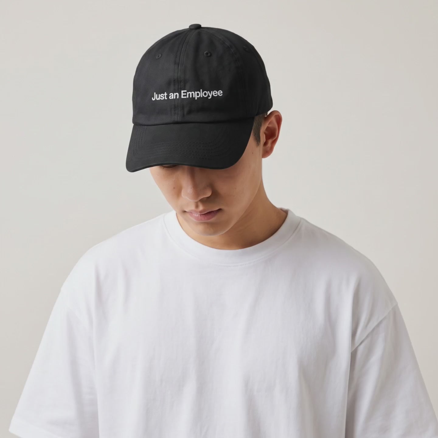 Video: model in a white tee wearing the Just an Employee black cap, head tilted down