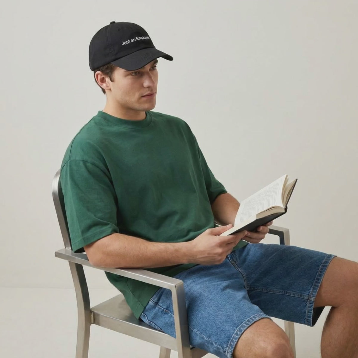 Video: man in a green tee reading a book while wearing the Just an Employee cap